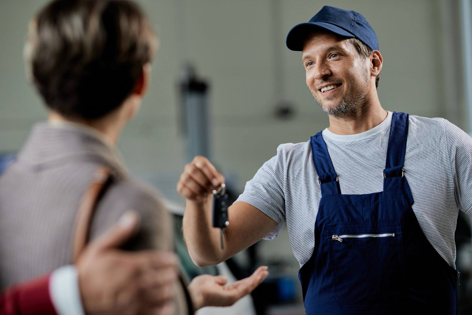 Happy mechanic giving car key to his customer in auto repair shop