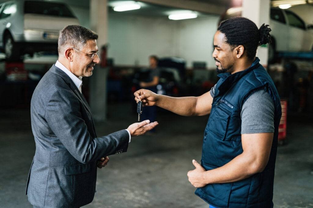 Happy black auto mechanic giving car key to his customer